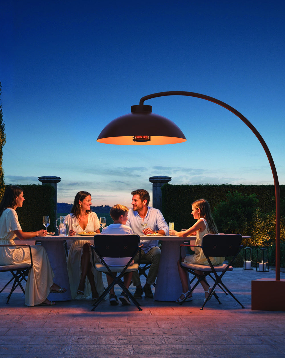 Heatsail DOME in Terra boven een eettafel op het terras bij avondlicht