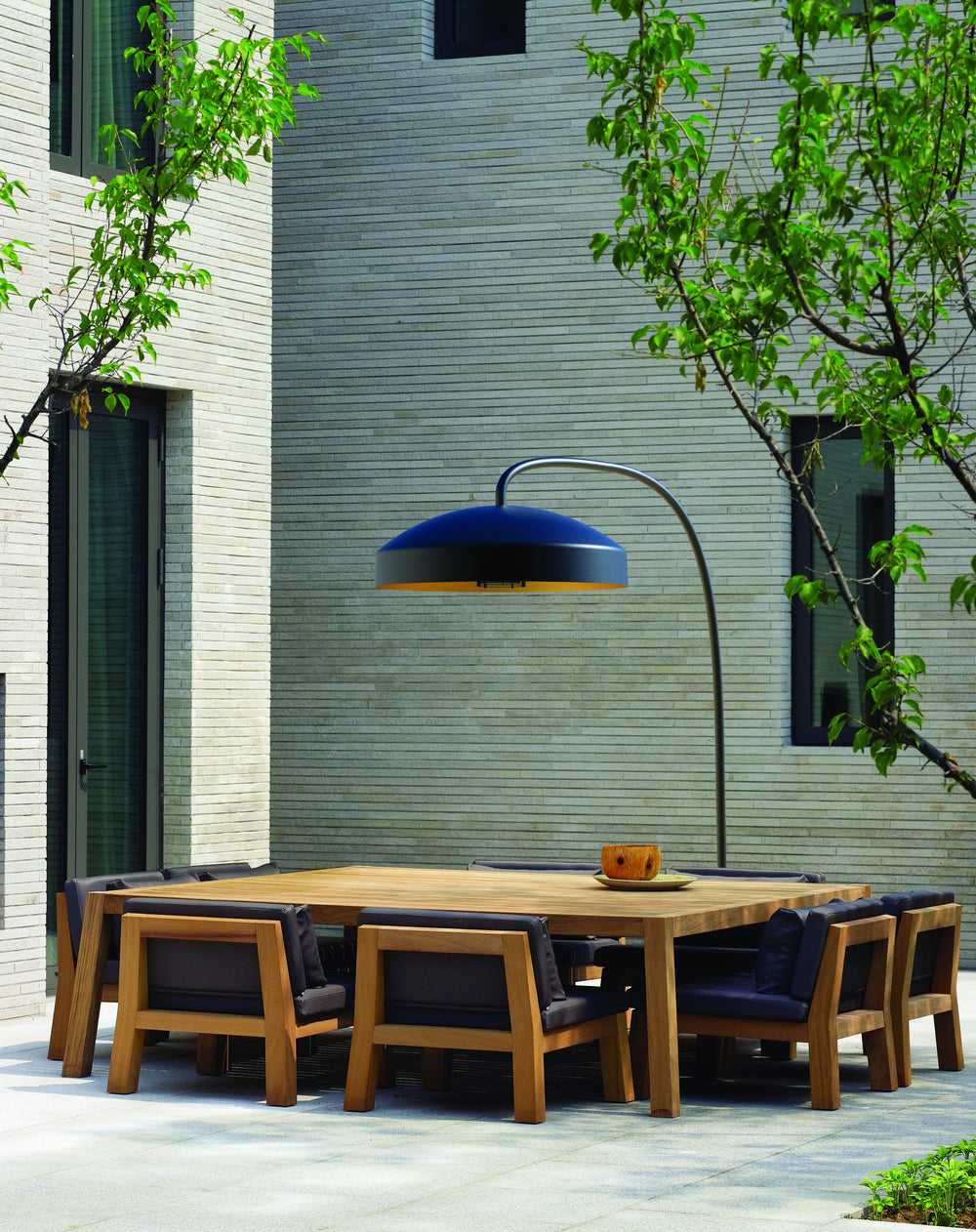 Heatsail DISC hangende terrasheater boven een houten tuintafel in een groene patio
